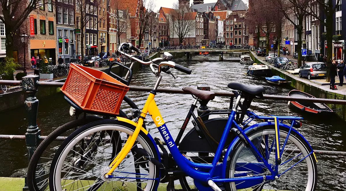 În Olanda nu se mai organizează referendumuri consultative. Fotografie cu orașul Amsterdam, capitala Olandei, cu două biciclete în prim-plan