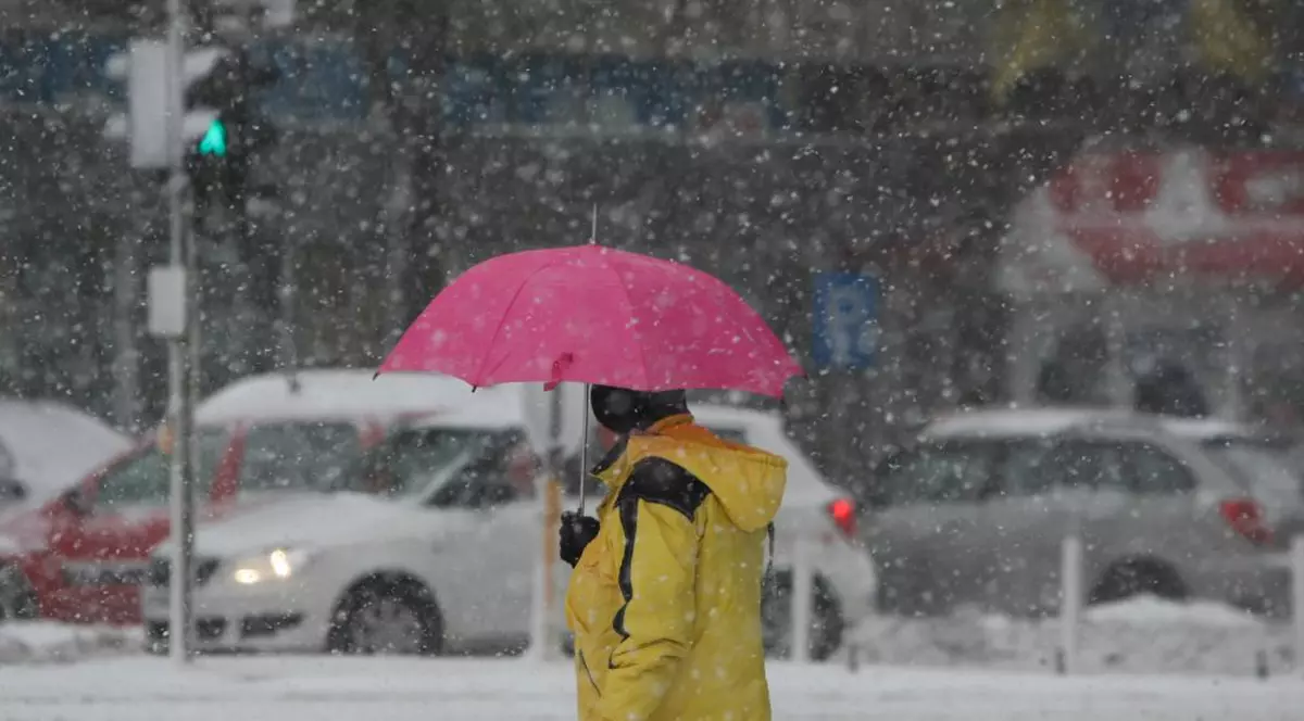 Vremea în București, pe 29 ianuarie. Un bărbat cu geacă galbenă ține o umbrelă roz, în plină ninsoare