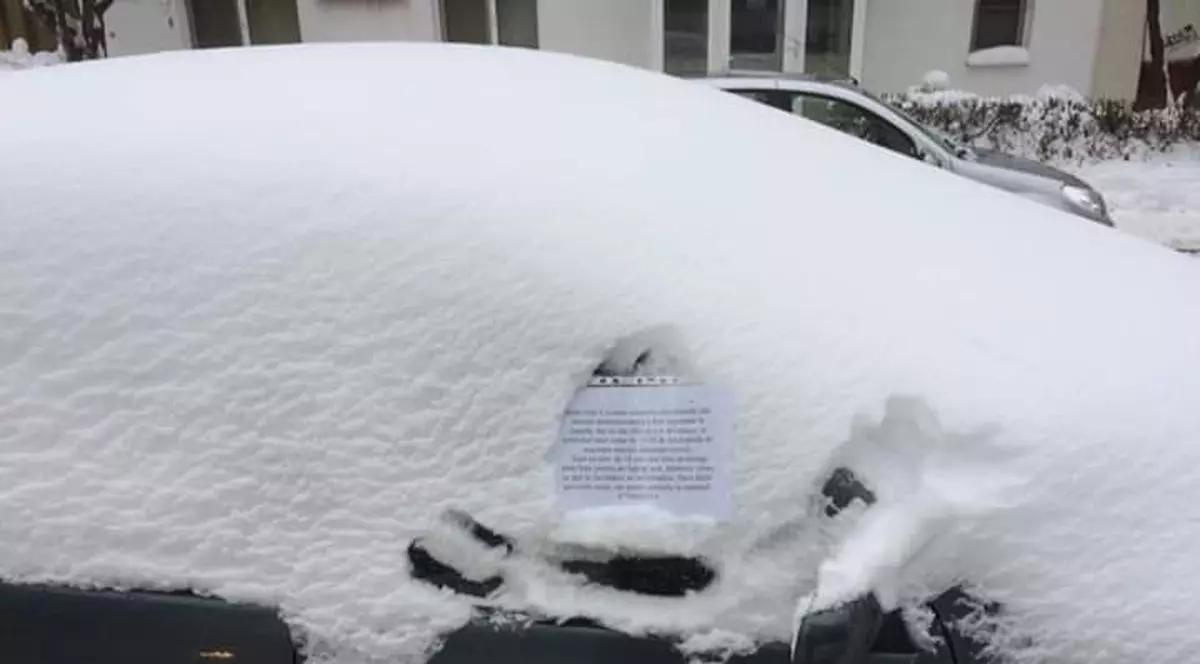 Un tânăr curăță zăpada de pe mașinile din parcare pentru un laptop nou