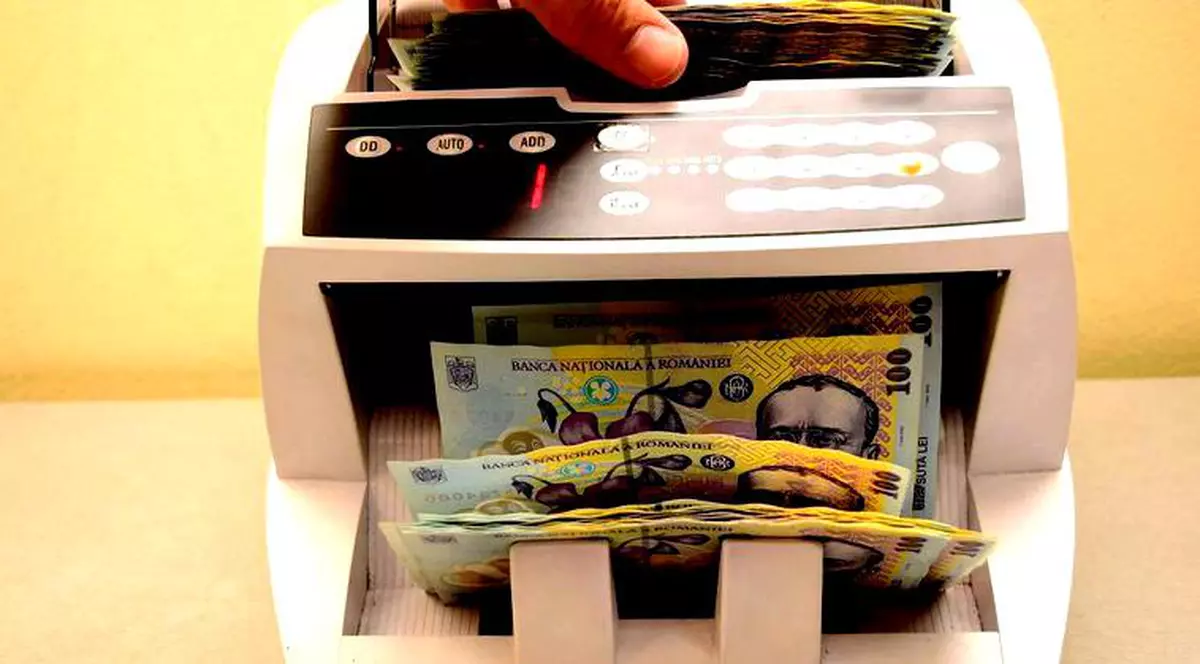 Guvernul a colectat cu 21 de miliarde de lei mai puțin decât și-a propus, iar diferența nu poate fi recuperată până la final de an. Aparat de numărat bani cu teancuri de bancnote în el