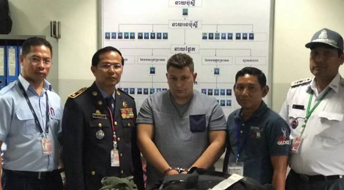 Un român a fost prins cu cinci kilograme de droguri pe un aeroport din Cambodgia. A mai avut un complice român. Ce pedeapsă riscă. Olaru (centru), între polițiștii care l-au reținut