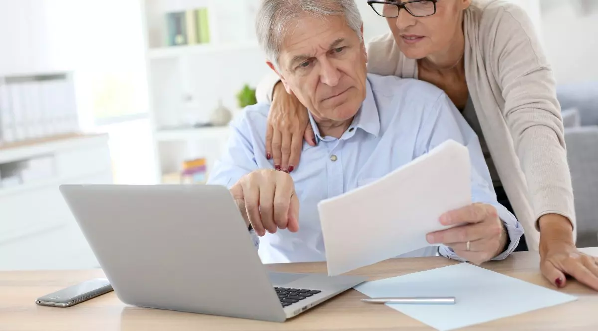 Românii nu ar trebui să renunțe la Pilonul II de pensii, consideră specialiștii. Cuplu de pensionari care calculează taxele în fața unui calculator