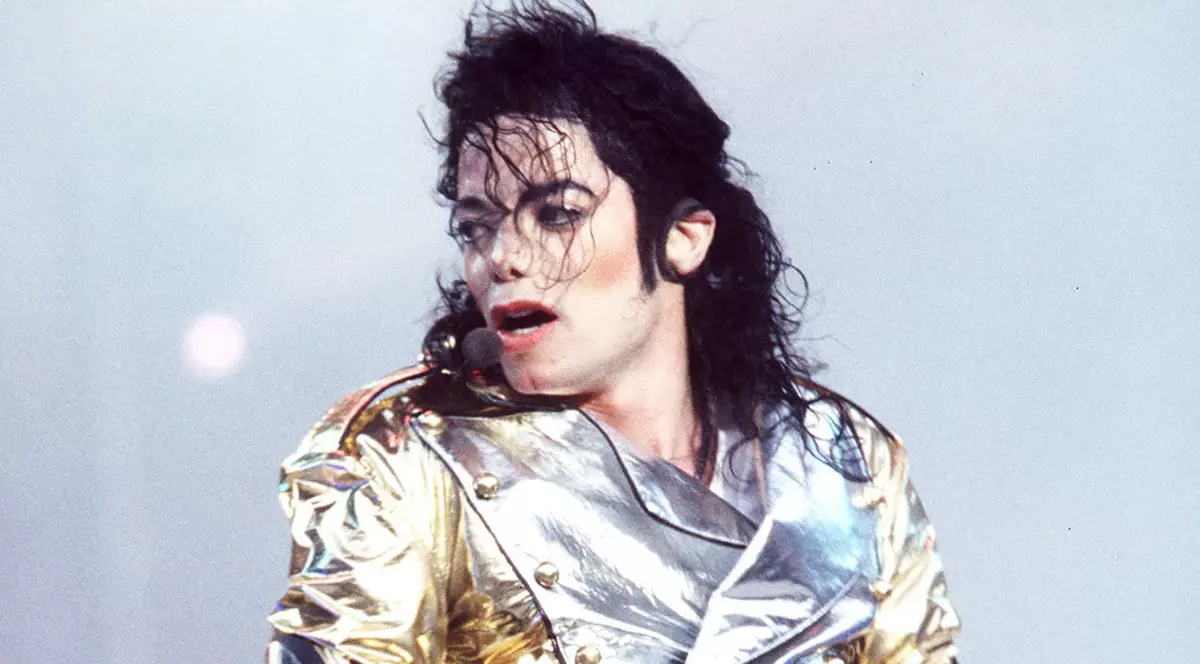 Michael Jakson, îmbrăcat într-o jachetă aurie lucioasă, dansâns pe scenă, cu părul în fața ochilor