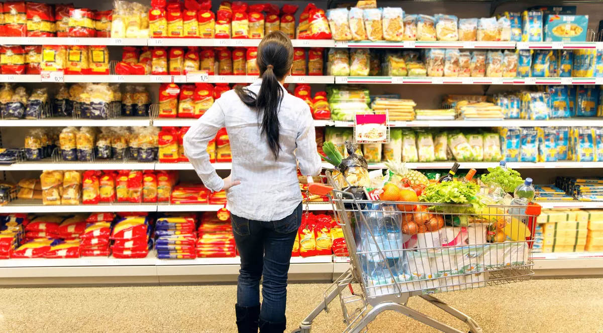 ANPC propune plafonarea prețurilor la produsele de strictă necesitate și raționalizarea lor. Femeie la raft cu un coș de cumpărături