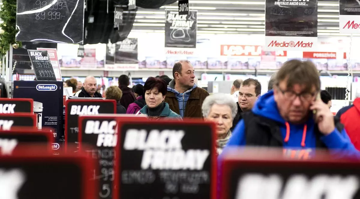 Black Friday, o afacere de 300 de milioane de euro în România. Oameni la coadă, cu semne de promoții privind Black Friday pe lângă ei