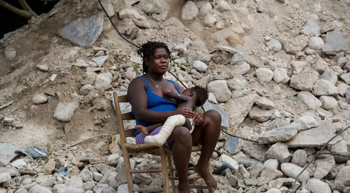 O mamă își alăptează fiul în fața ruinelor locuinței sale | Foto: EPA