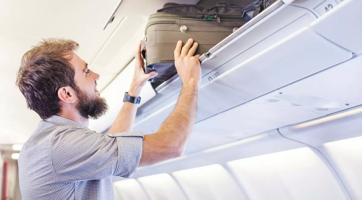Un bărbat introduce un troller în spațiu de bagaje din interiorul unui avion.