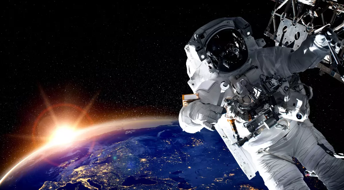 De ce se antrenează cosmonauții în apă - Imagine cu un cosmonaut care efectuează o intervenţie tehnică în spaţiul cosmic, având în fundal Pământul şi Soarele.