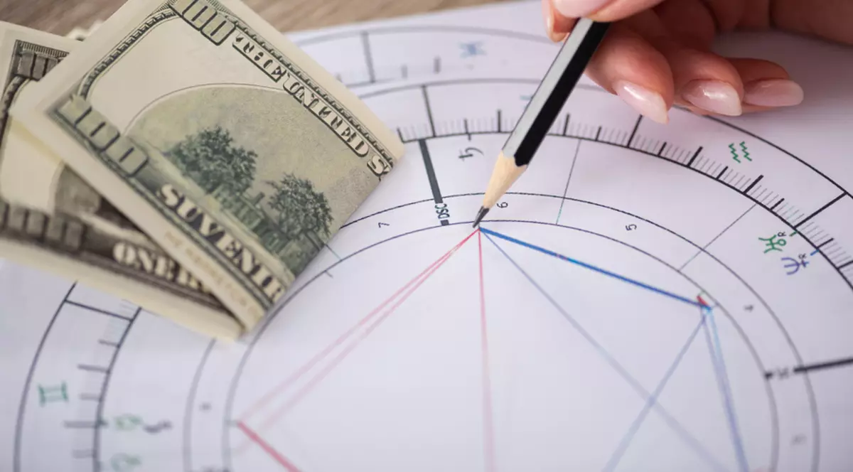 Zodii cu noroc la bani în această toamnă - Imagine cu o persoană care întocmeşte o astrogramă şi o bancnotă de 100 de dolari.