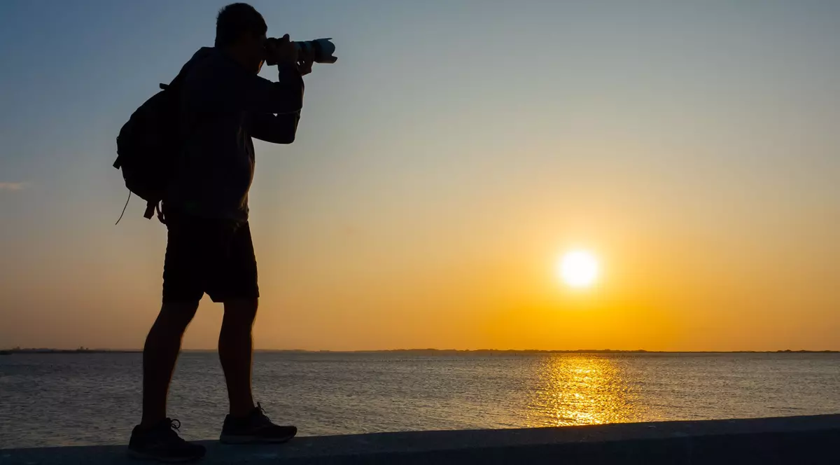 Aparate foto la ofertă de Black Friday 2022 - Imagine cu un bărbat aflat pe malul mării, care fotografiază un apus de soare