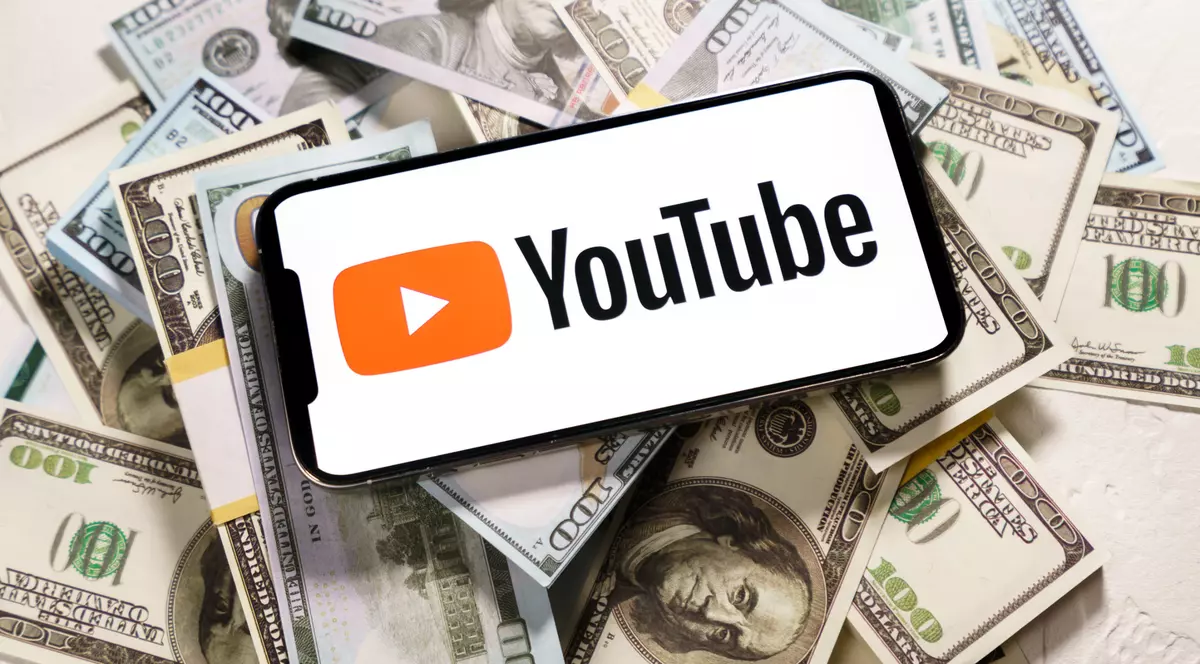 Cum poţi să câștigi bani pe YouTube - Imagine cu un telefon ce are pe ecran sigla YouTube şi este aşezat pe un teanc de bani