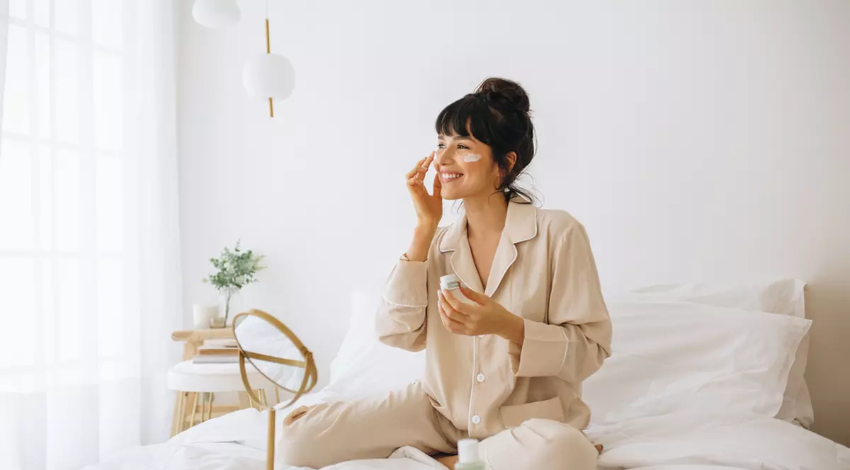 Produse cosmetice la reducere în oferta Notino.ro de azi, 20 decembrie - Imagine cu o tânără care îşi face programul de ifrumuseţare dimineaţa, în pat
