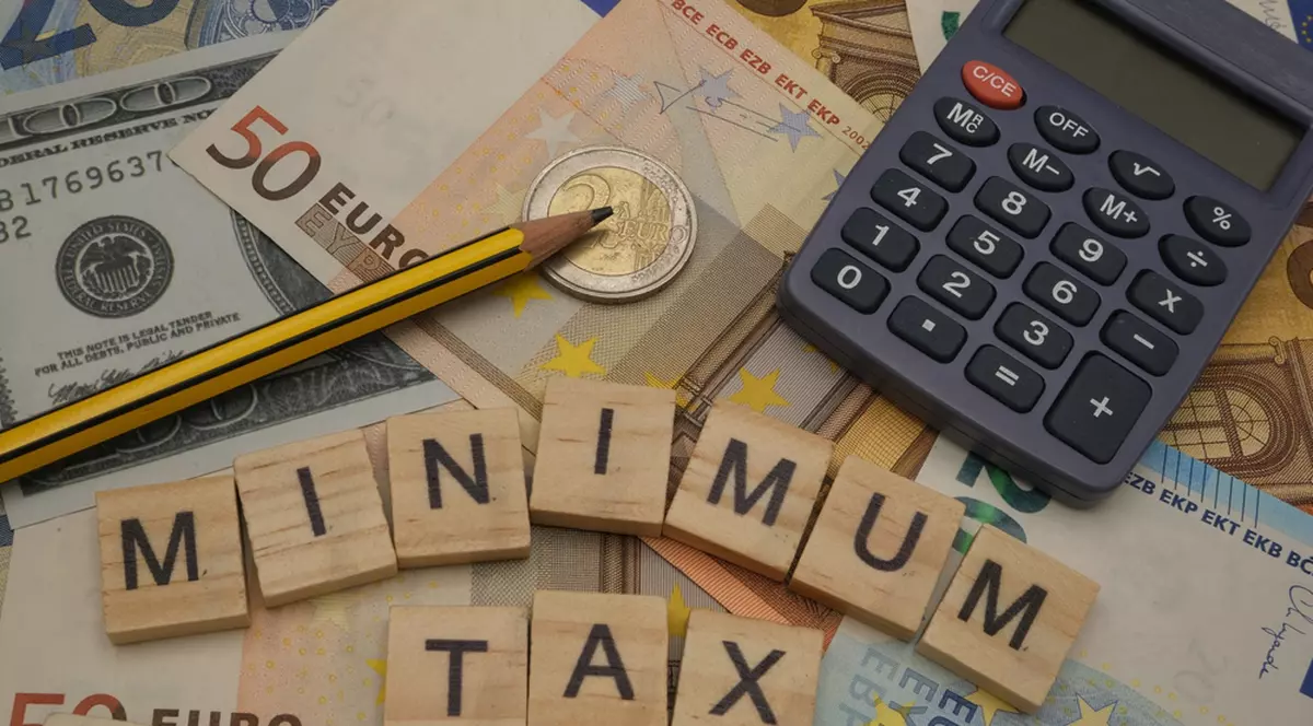 Care sunt ţările cu cele mai mici taxe din Europa - Imagine cu literele care formează cuvintele Minimum Tax alături de un calculator şi un creion pe un teanc de euro