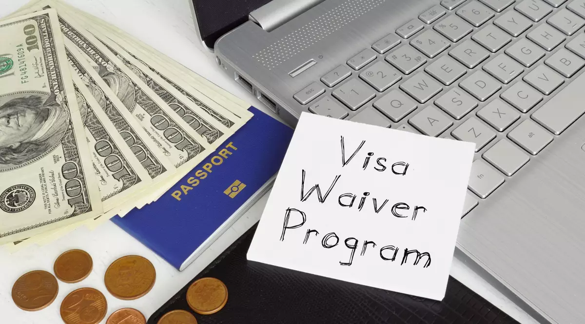 Ce este Visa Waiver și ce țări fac parte din program - Imagine cu bani, monede şi bacnote, un paşaport, un laptop şi un post it pe care este scris Visa Waiver Program