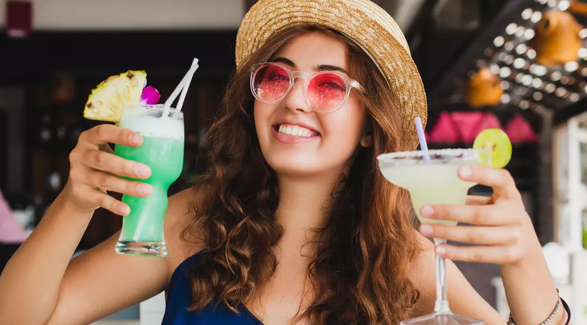Rețete de cocktailuri de vară cu prosseco și fructe - Imagine cu o tânără îmbrăcată de plajă care ţinâ în mâini câte un cocktail