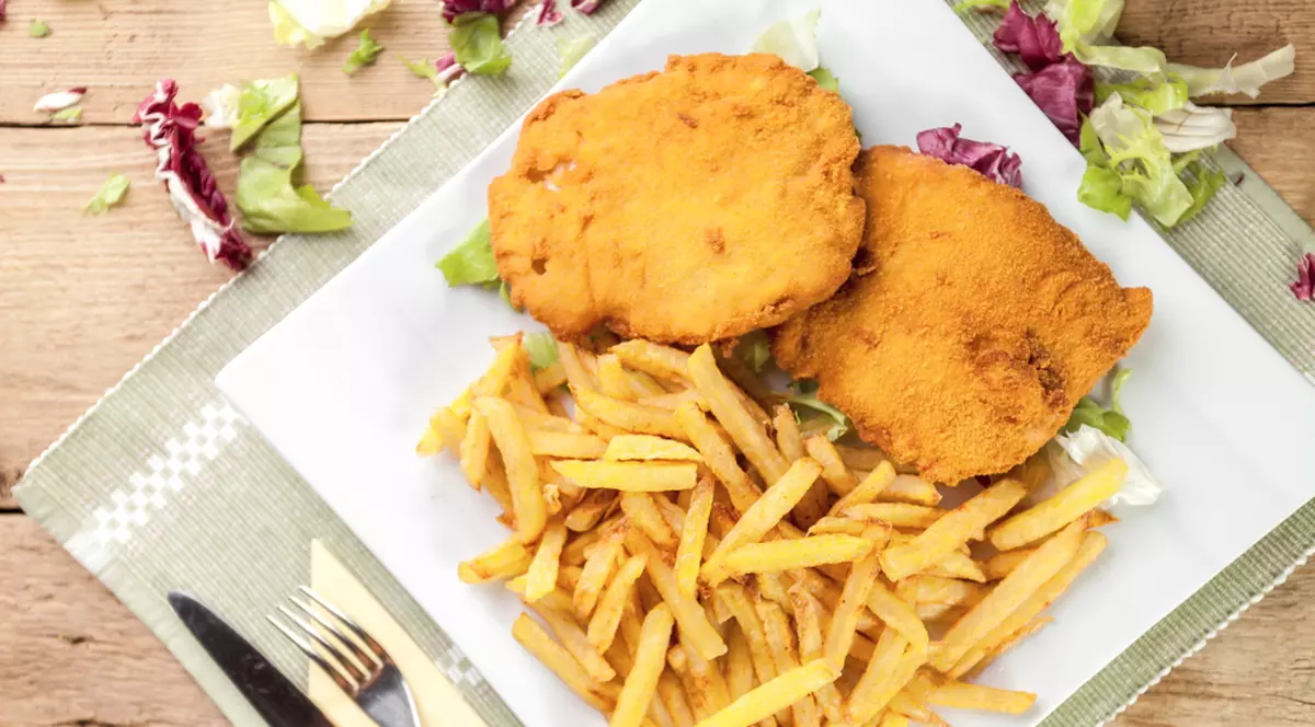 Patru reţete de carne pane - Imagine cu o farfurie pe care se află două şniţele cu cartofi prăjiţi.