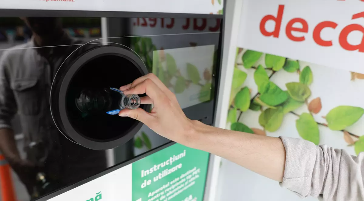 Cum funcţionează Sistemul de Garanţie-Returnare - Imagine cu o persoană care introduce o sticlă goală de plastic într-o maşnă de recuperare a ambalajelor