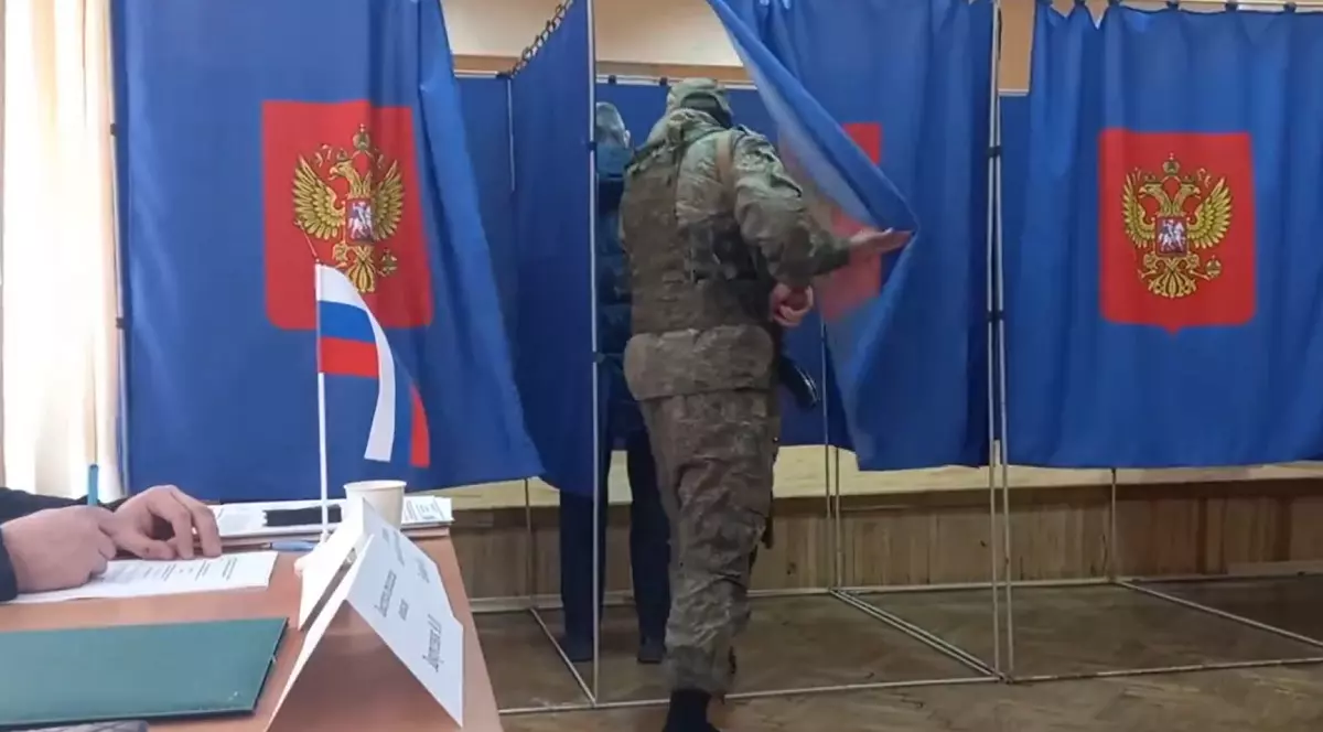 Un soldat rus cu mitralieră și cagulă, filmat când intră peste alegători în cabina de vot. „Așa a fost toată ziua”