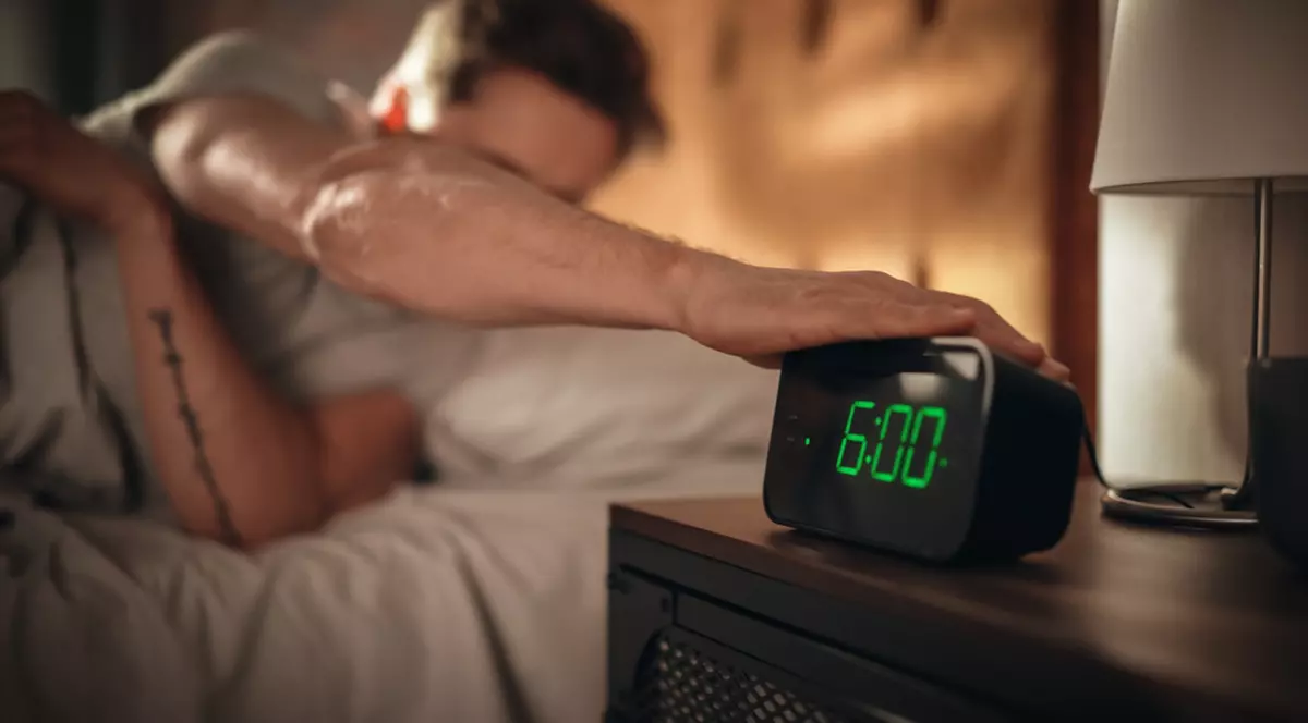 Beneficii ale trezitului devreme - Imagine cu un bărbat care opreşte ceasul deşteptător, la ora 06.00.