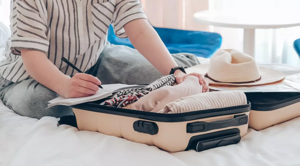 O femeie isi pune hainele intr-un troller de mici dimensiuni, consultand lista facuta inainte