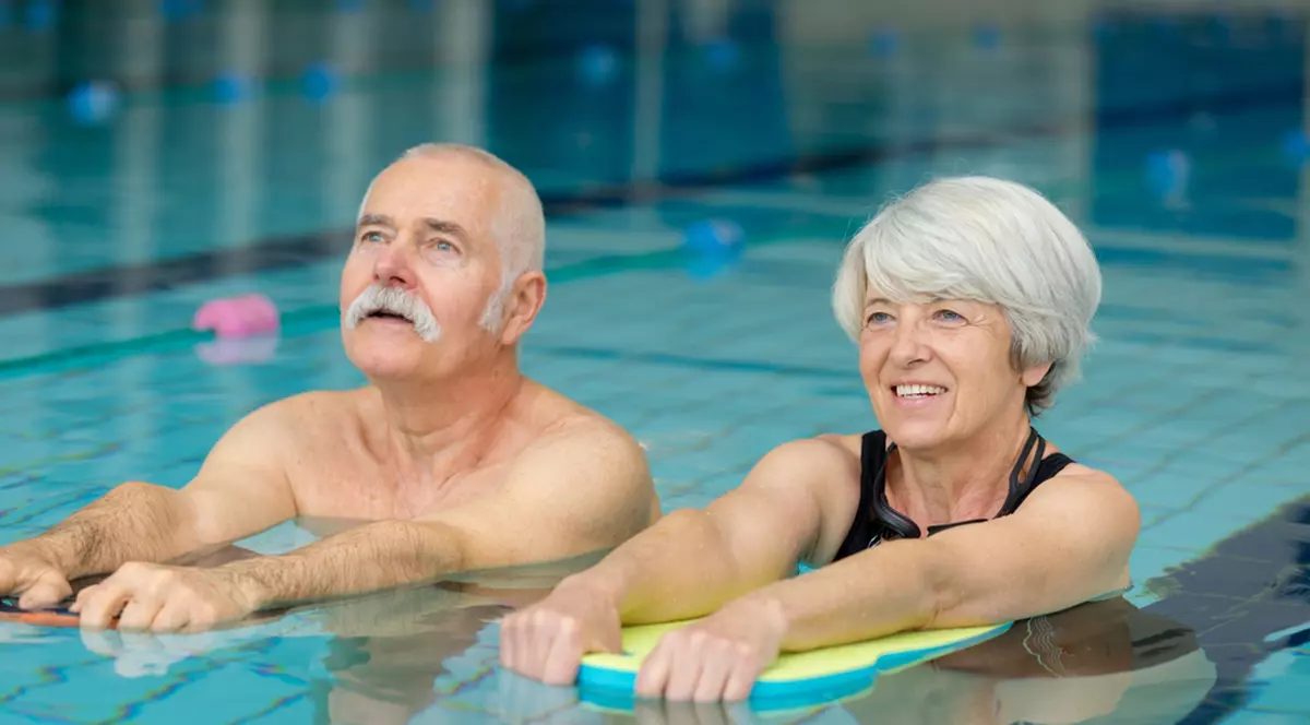 Exerciţii fizice potrivite pentru persoanele în vârstă- Un barbat si o femeie in varsta fac aerobic intr-o piscina acoperita