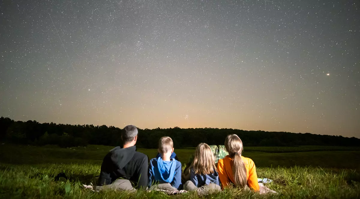 Perseidele – când are loc ploaia de meteoriți în 2024 - Imagine cu o familie, tatăl, mama şi doi copii, urmărind o ploaie de meteori, pe un cer înstelat