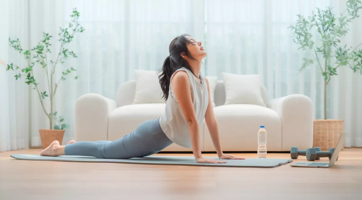 Ce exerciții de yoga să faci pentru un somn odihnitor - Imagine cu o tânără care face yoga în propria locuinţă