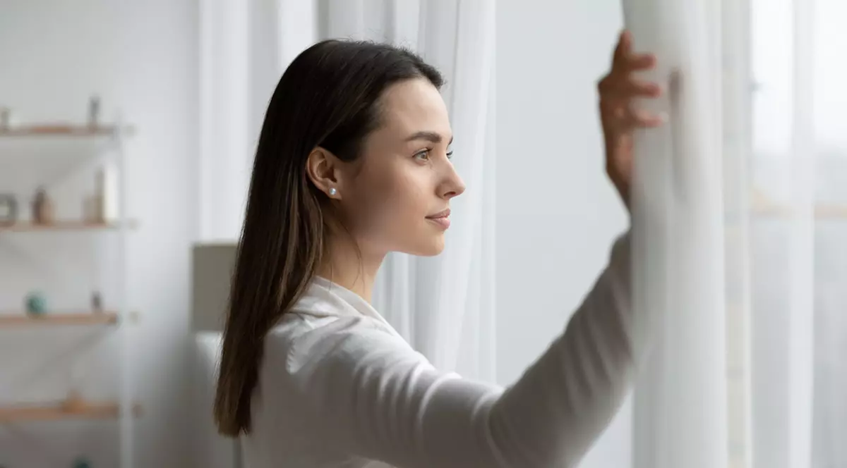 Ce presupune stilul de viaţă olandez Niksen - Imagine cu o tânără femeie îmbrăcată în alb, care priveşte pe o fereastră.
