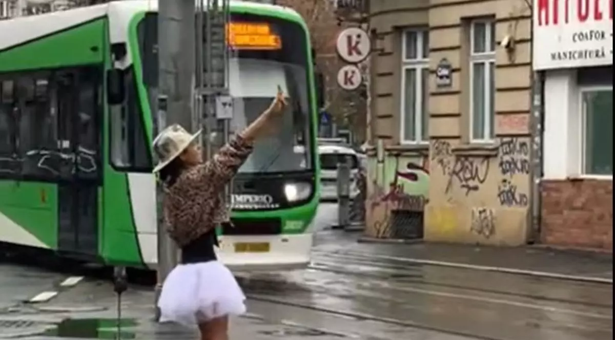 femeie in tutu rox dansand pe strazile bucurestiului cu un tramvai care trece prin spatele ei