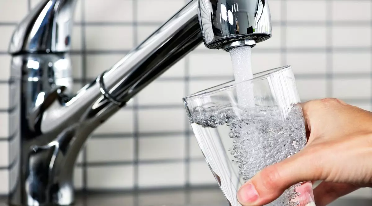 femeie care umple un pahar cu apă de la robinetul din bucătărie