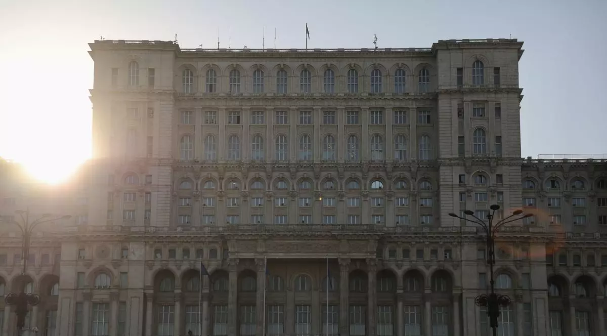 Prim plan cu Palatul Parlamentului din București, cu soarele care strălucește puternic în colțul din stânga-sus al clădirii
