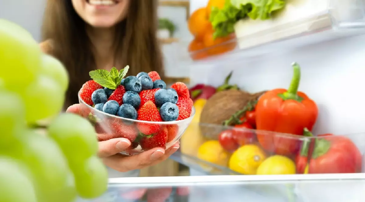 O femeie ia din frigider un bol cu fructe de padure