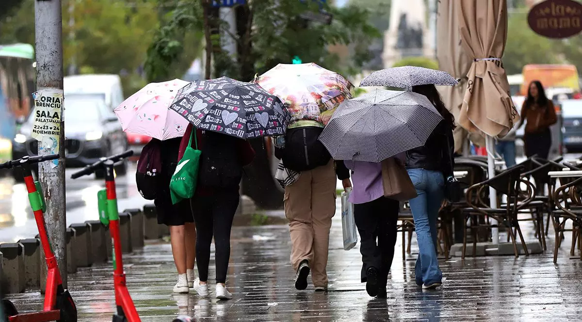 Femei care se protejează de ploaie cu ajutorul umbrelelor.