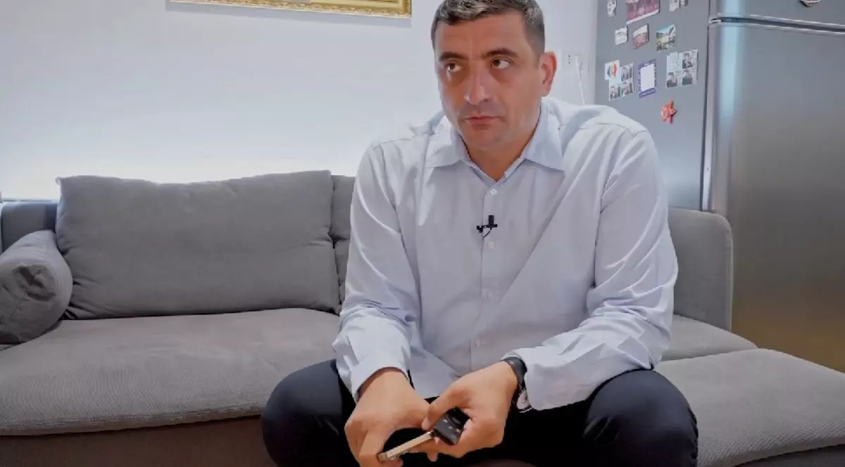 George Simion, în timp ce stă pe canapeaua din casa sa, îmbrăcat într-o cămașă albastră, cu telefonul în mână