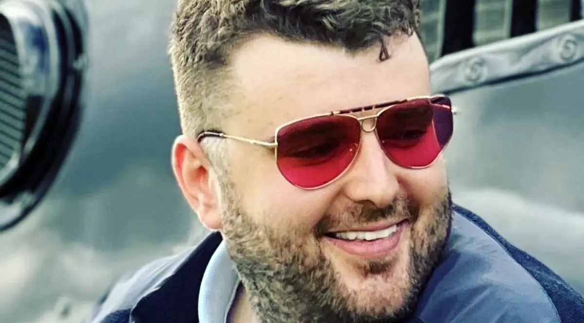 prim plan cu Victor Micula, purtând ochelari de soare cu lentile roșii, o cămașă și un sacou, zâmbind