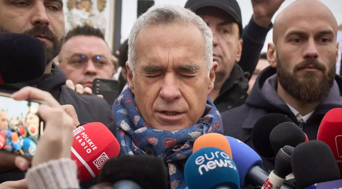 Călin Georgescu, candidatul de extremă dreapta, în timpul unu interviu, cu microfoane lângă el, cu un fular de culoare albastră la gât, și cu ochii închiși