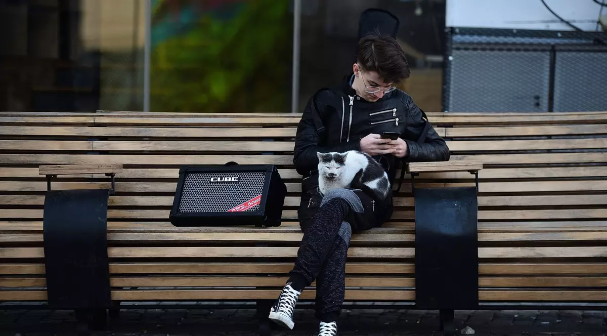 Un tânăr își verifică telefonul, ținândd în brațe o pisică