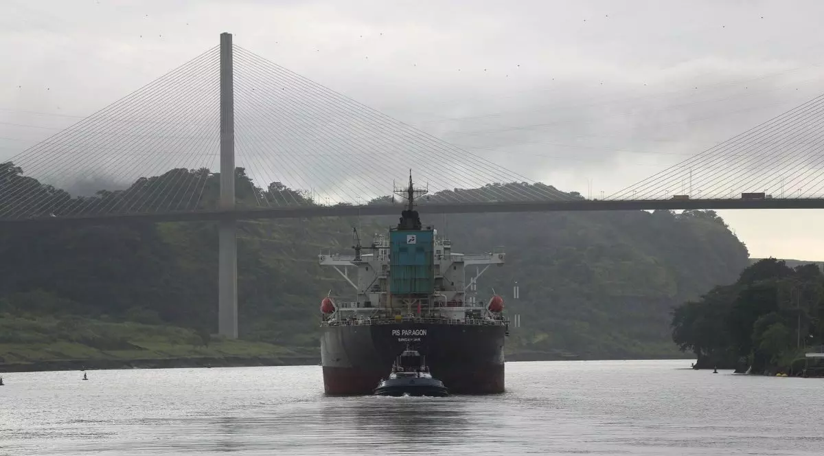 o navă trece prin canalul panama. in departare se vede un pod