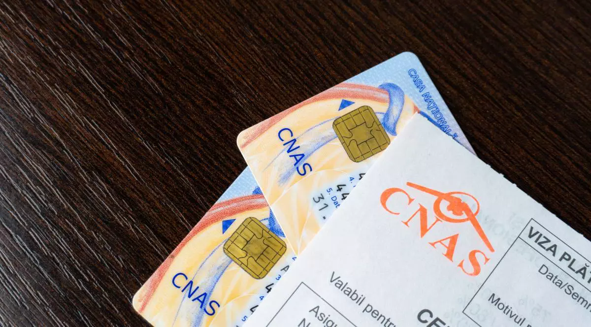doua carduri de sanatate cnas pe un birou, deasupra un bilet de trimitere cnas