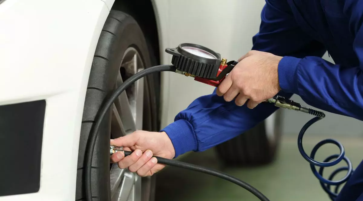 Un bărbat, care ține în mână o pompă de aer, verifică presiunea din anvelopele unei mașini de culoare albă