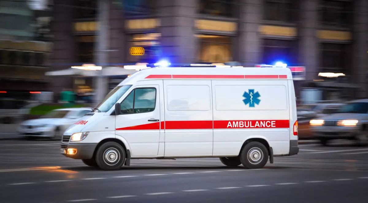 O mașină a Ambulanței în trafic, cu luminile aprinse, într-un fundal neclar.
