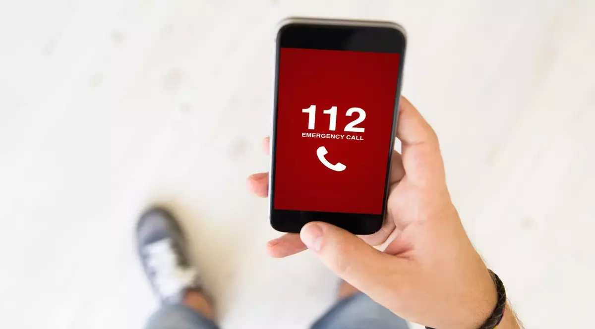 Bărbat care ține în mână un telefon pe ecranul căruia este afișat numărul unic de urgență 112.