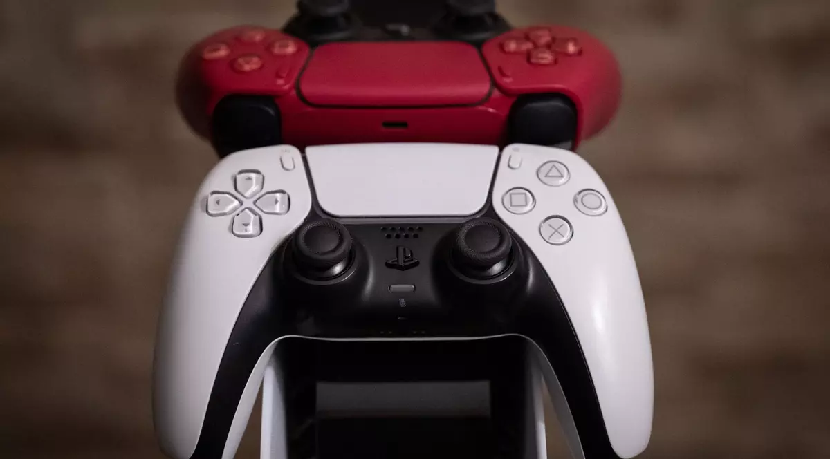 Două controllere de PlayStation 5, unul alb, unul roșu, așezate pe un stativ.