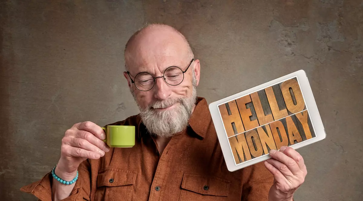 Curiozităţi despre ziua de luni - Imagine cu un bărbat care ţine într-o mână o ceaşcă de cafea şi în cealaltă un afiş pe care scrie Hello Monday.
