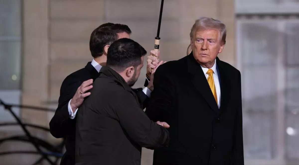 donald trump imbracat cu o camasa alba si palton negru in timp ce da mana cu volodimir zelenski. in spatele lor este emanuel macron