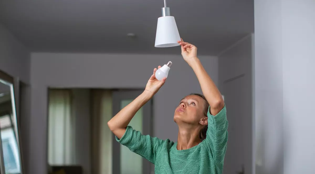Femeie care schimbă becul în casa ei - Foto Profimedia