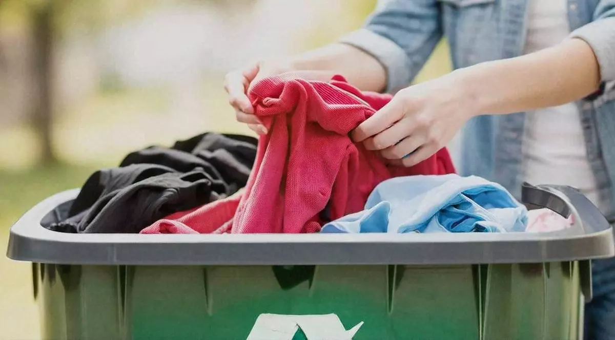 persoana care pune haine intr-un tomberon pentru reciclarea deseurilor textile