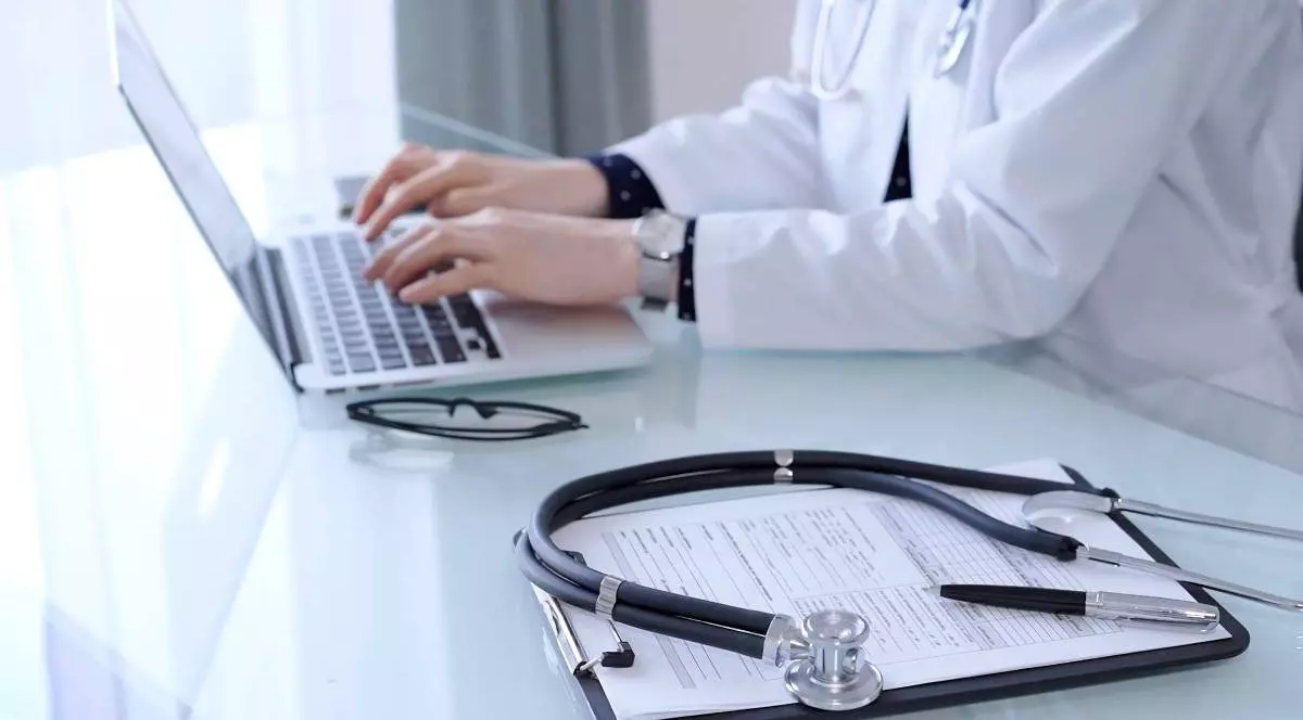 medic care tasteaza la computer, pe masa are foi si un stetoscop