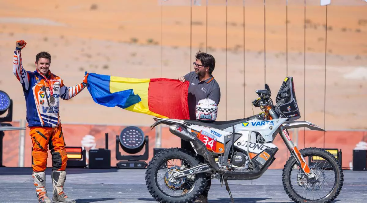 raider roman castigat dakar 2025 tine in mana drapelul romaniei, langa el este motocicleta sa