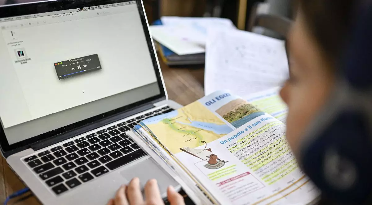 Un elev se uită pe manual, in fata unui laptop